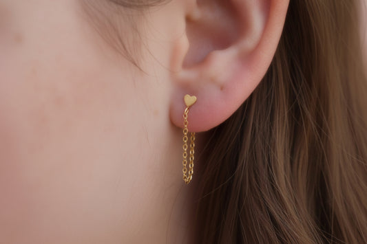 Gold heart-shaped earring worn on an ear with a blurred background