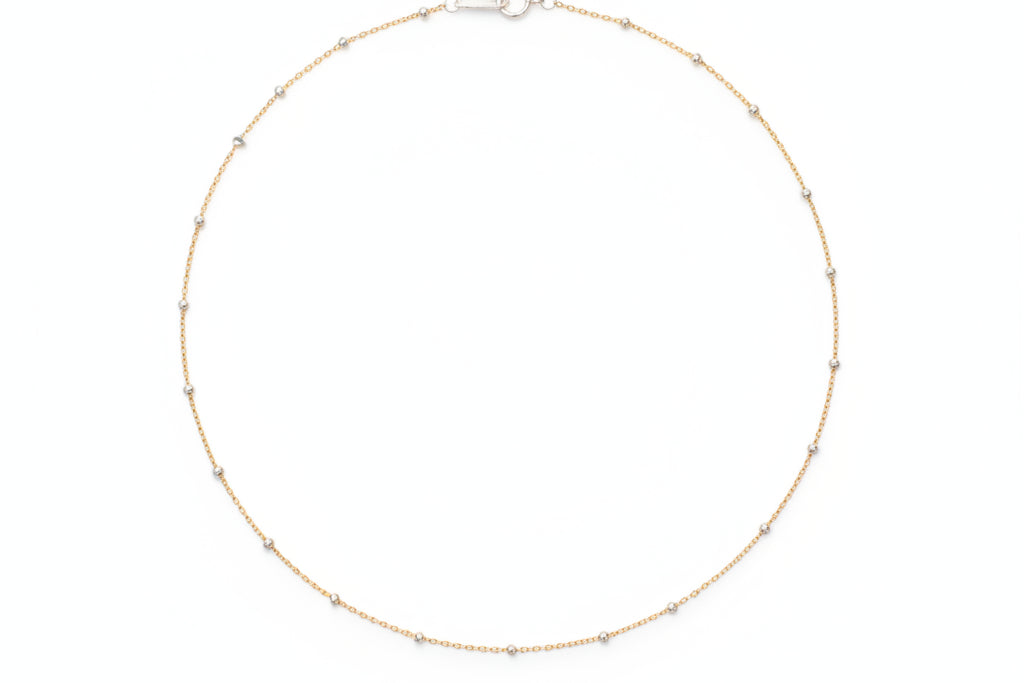 Gold necklace on a marble surface with flowers in the background
