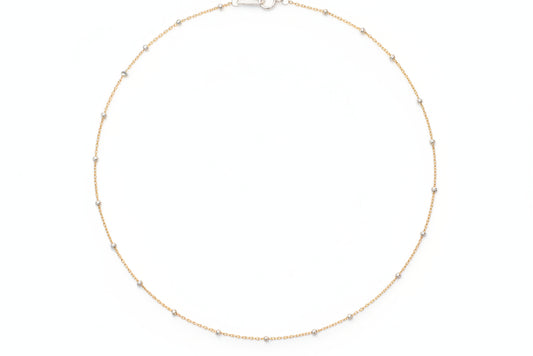 Gold necklace on a marble surface with flowers in the background