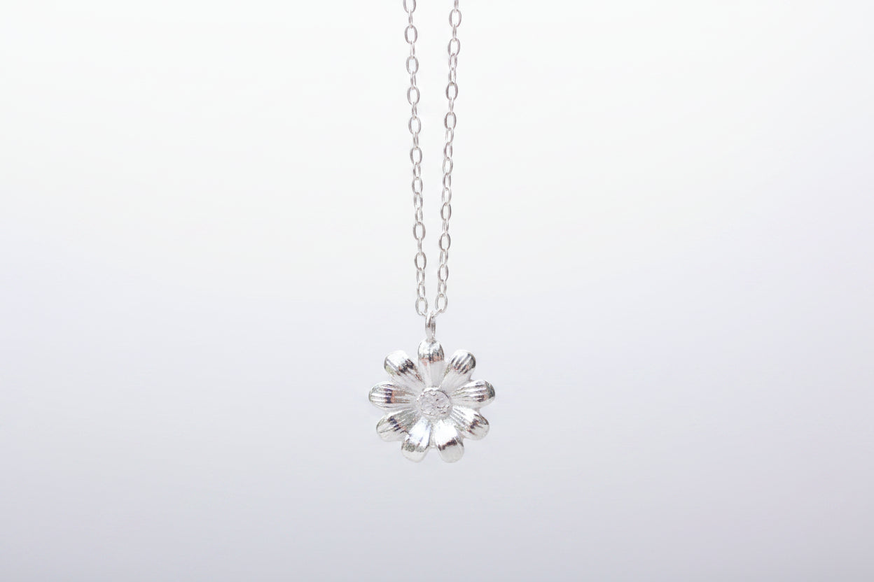 Silver flower pendant necklace on a marble surface with white flowers in the background