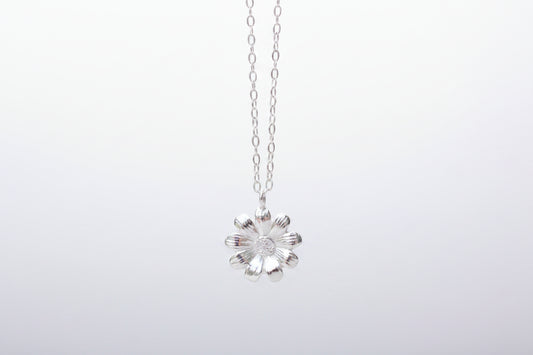 Silver flower pendant necklace on a marble surface with white flowers in the background