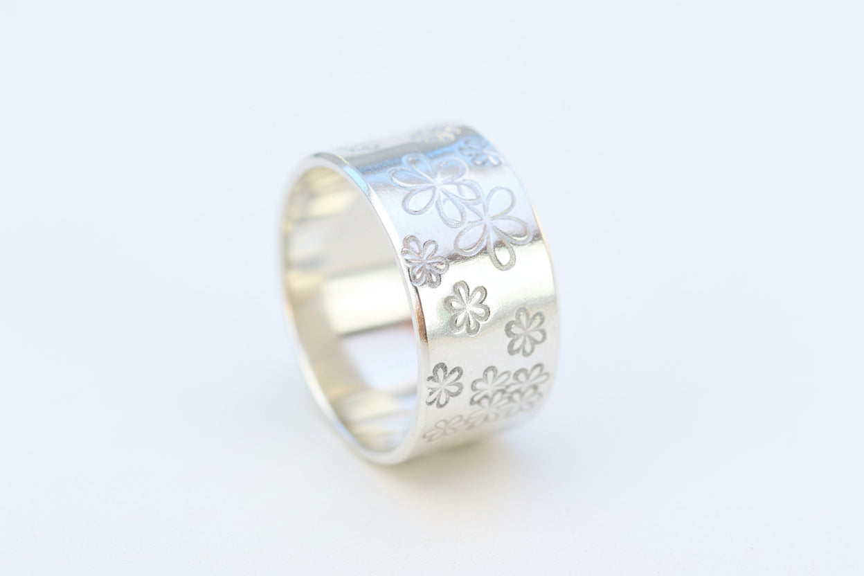 A sterling silver ring with a hand-stamped daisy design, displayed on a wooden surface.