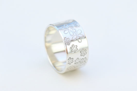 A sterling silver ring with a hand-stamped daisy design, displayed on a wooden surface.