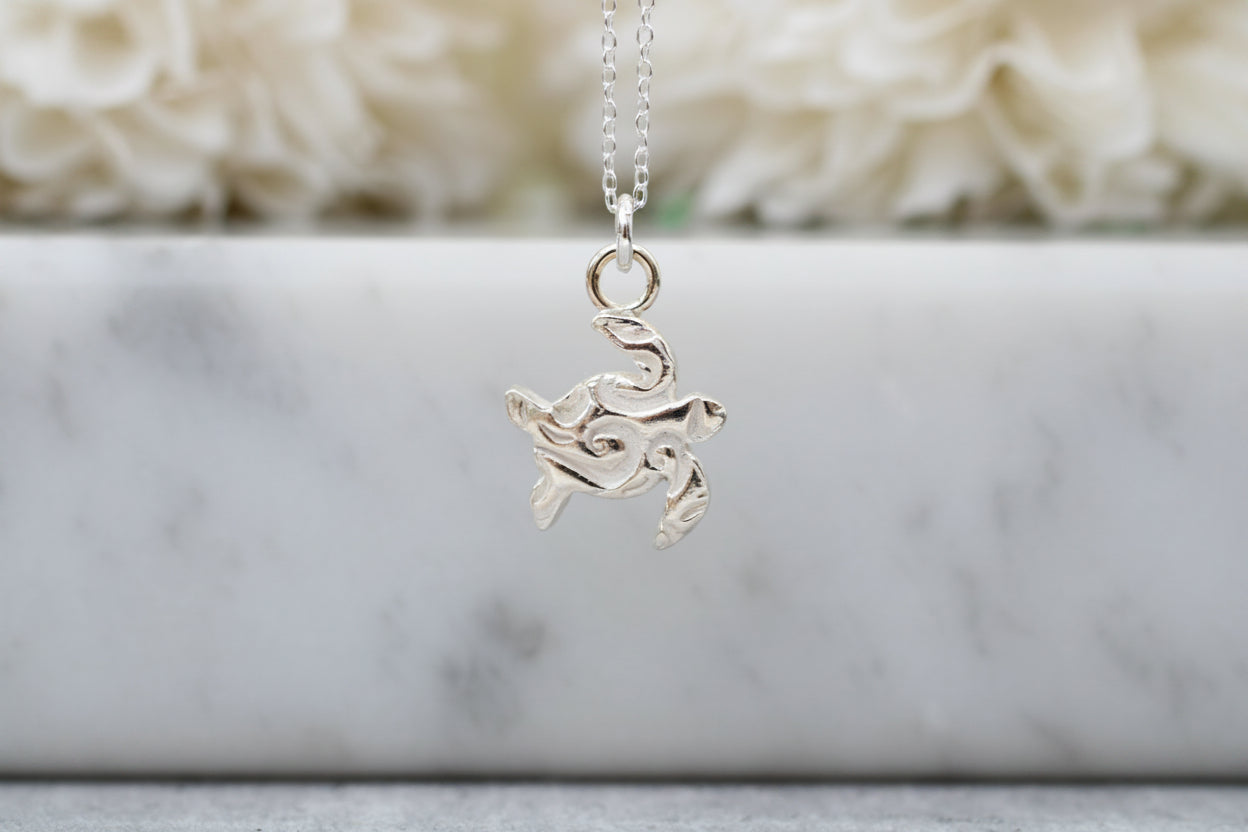 Silver turtle pendant necklace on a marble surface with a soft white background