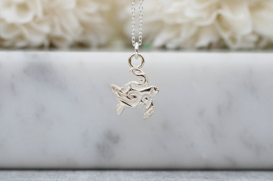 Silver turtle pendant necklace on a marble surface with a soft white background