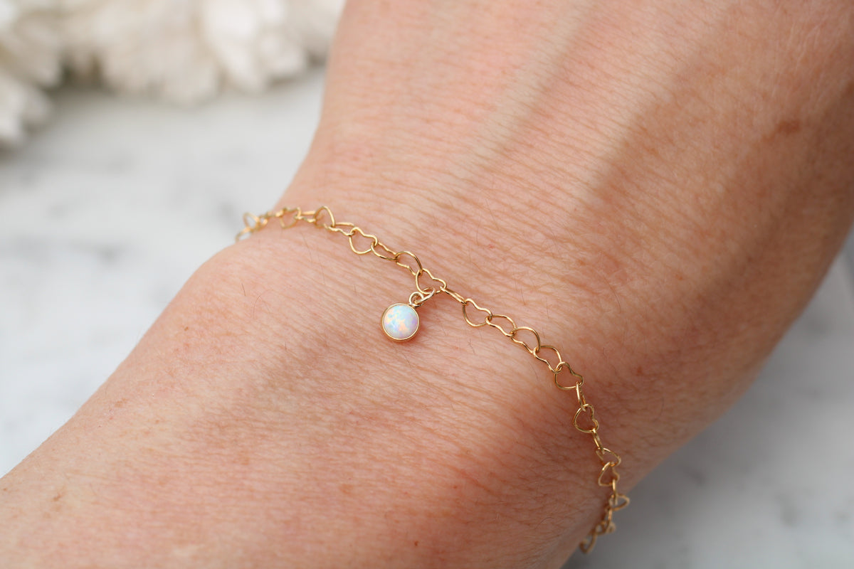 A delicate gold chain bracelet with a small white pearl charm, shown worn on a person's wrist against a soft, light marble background.
