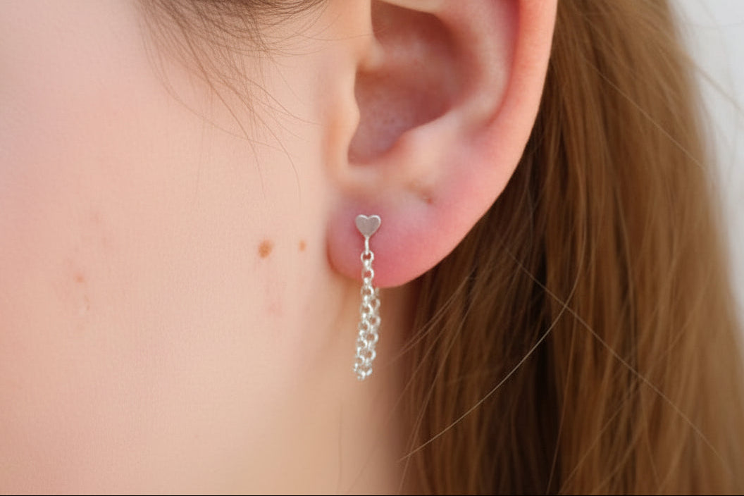 Close-up of an ear with a silver heart-shaped earring and a chain earring.