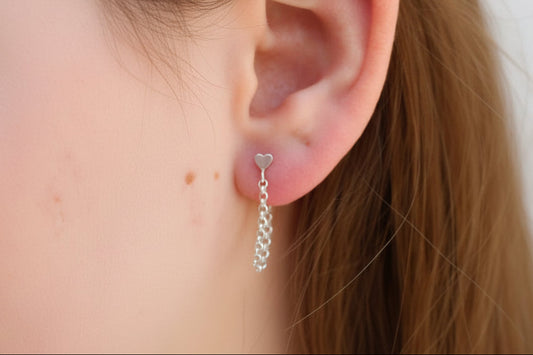 Close-up of an ear with a silver heart-shaped earring and a chain earring.