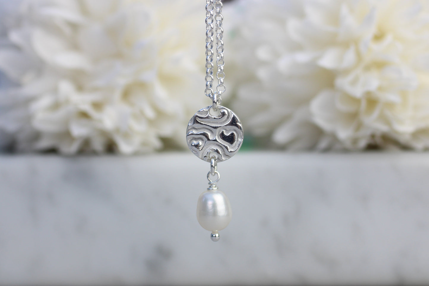 Silver necklace with a pearl pendant against a white floral background