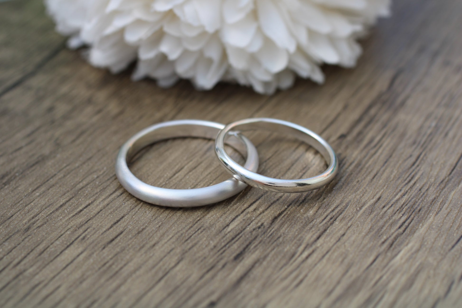 Two silver rings on a wooden surface with white flowers in the background