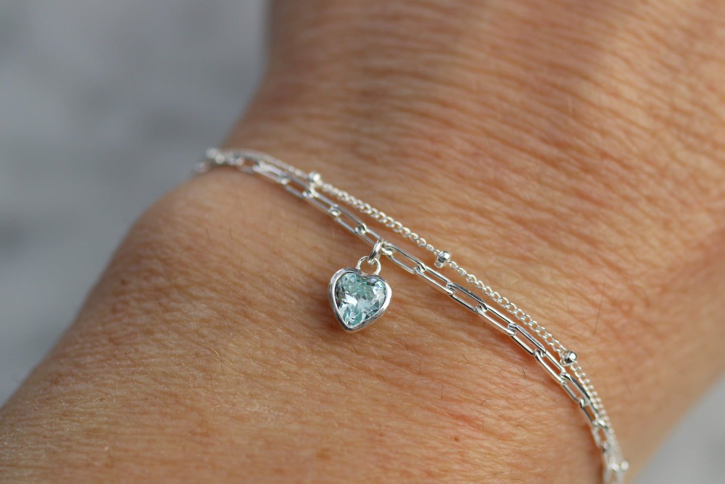Silver bracelet with a heart-shaped gemstone on a wrist against a neutral background