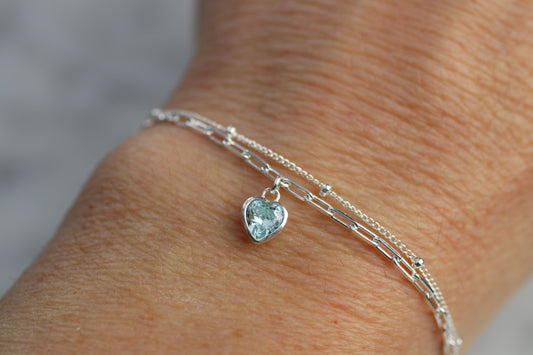 Silver bracelet with a heart-shaped gemstone on a wrist against a neutral background