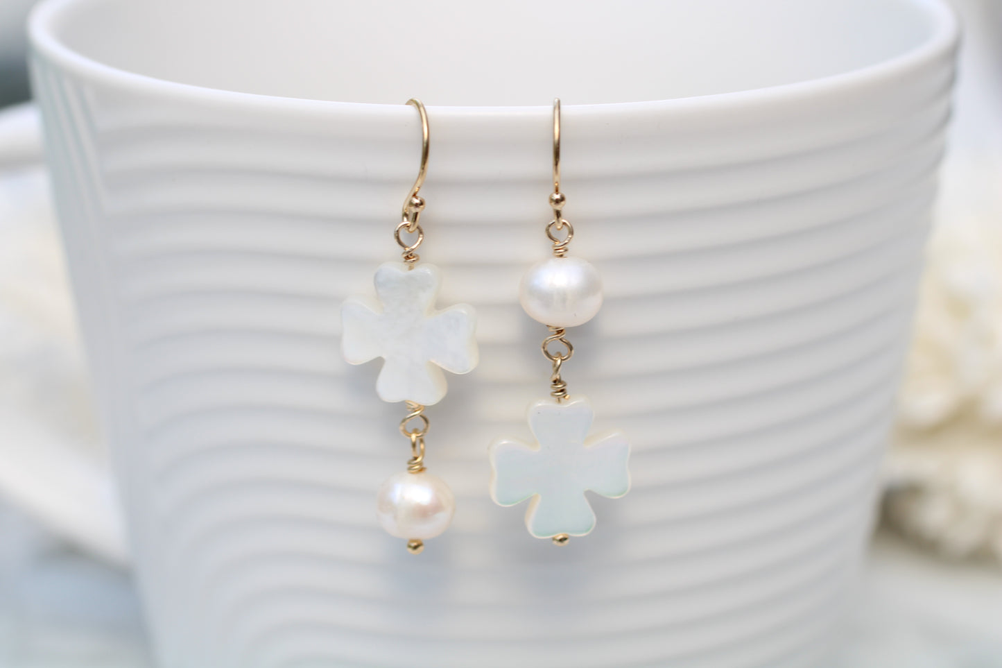 Pearl and flower-shaped earrings on a white cup