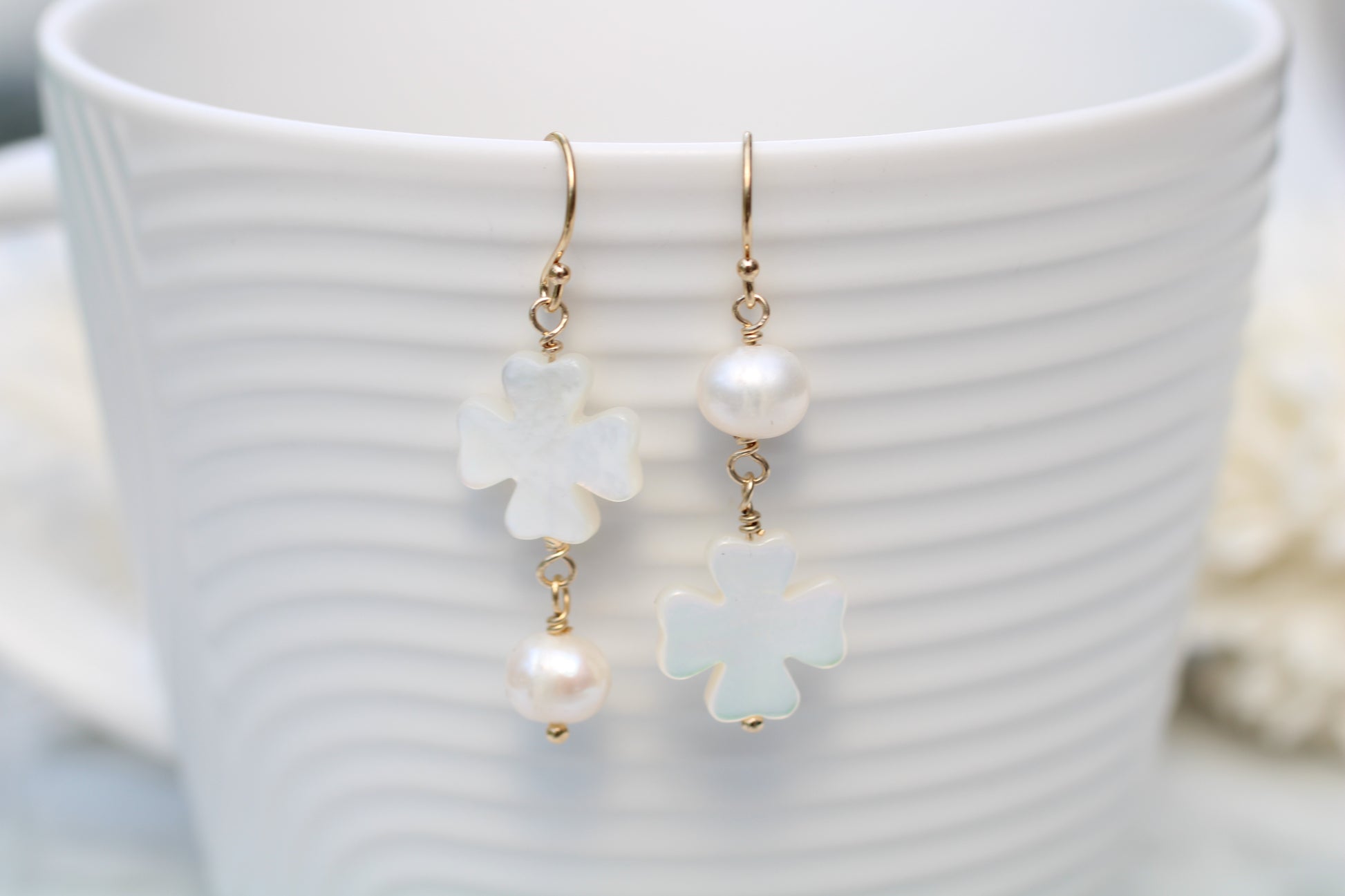 Pearl and flower-shaped earrings on a white cup