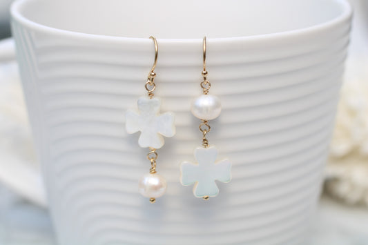 Pearl and flower-shaped earrings on a white cup