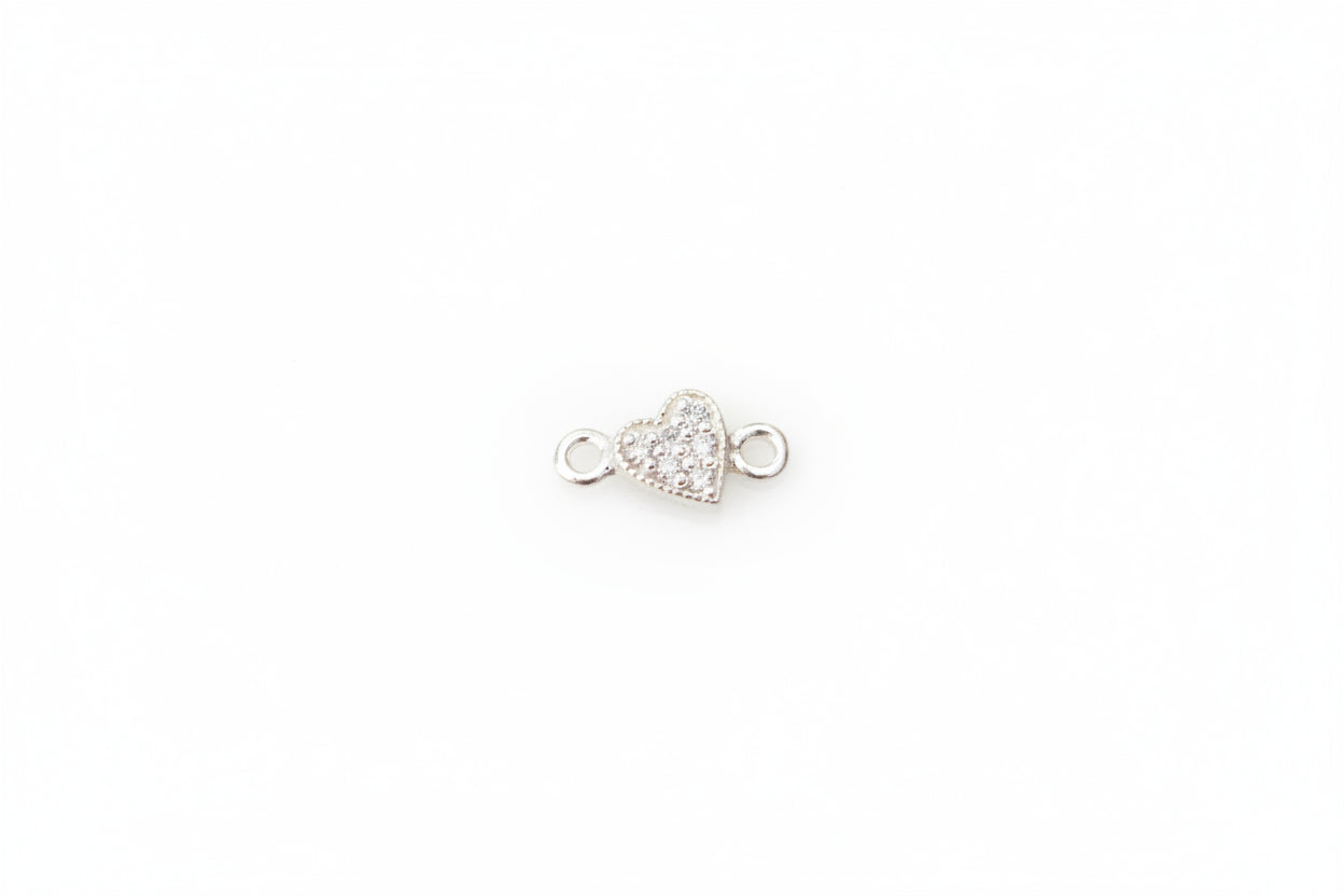 A small silver heart-shaped jewelry charm with moissanite displayed on a light gray marble surface.