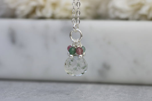 Necklace with a green teardrop pendant and small beads on a marble surface