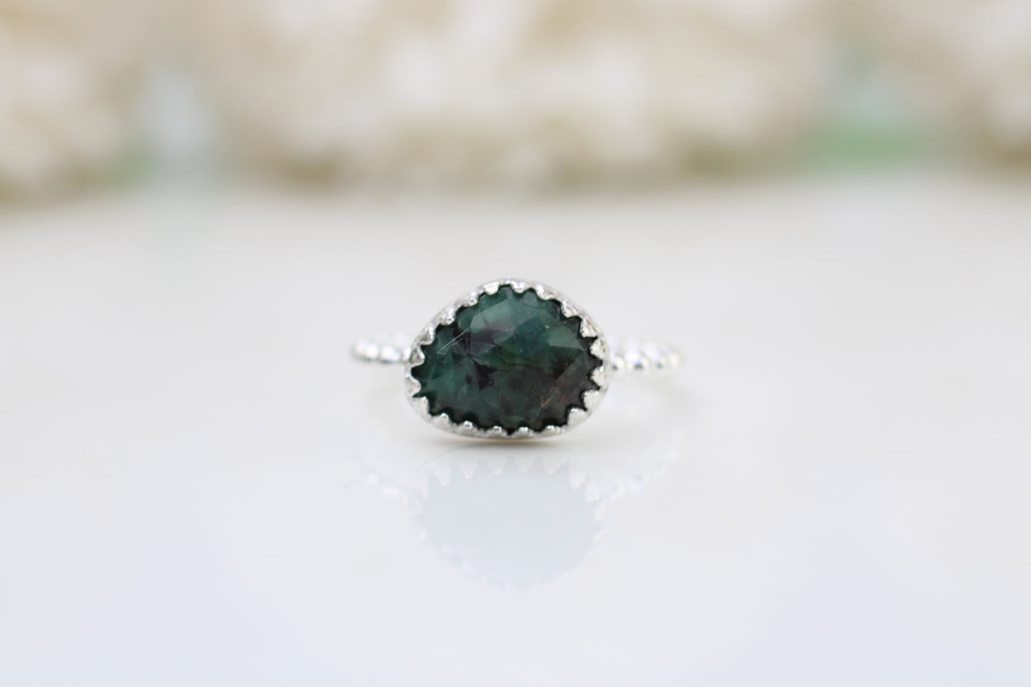 A ring with a rose-cut emerald gemstone set in a decorative bezel on a white background.
