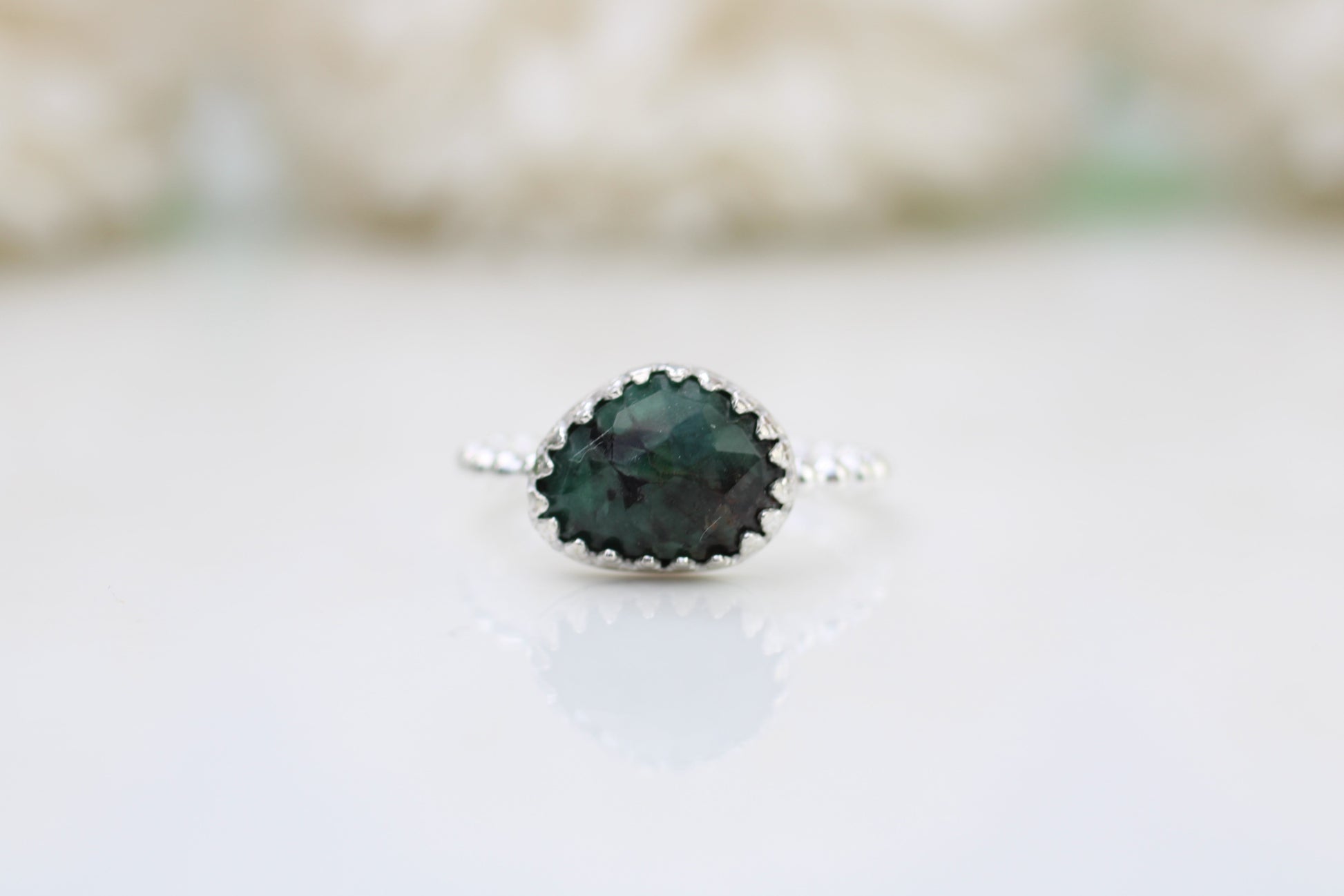 A ring with a rose-cut emerald gemstone set in a decorative bezel on a white background.