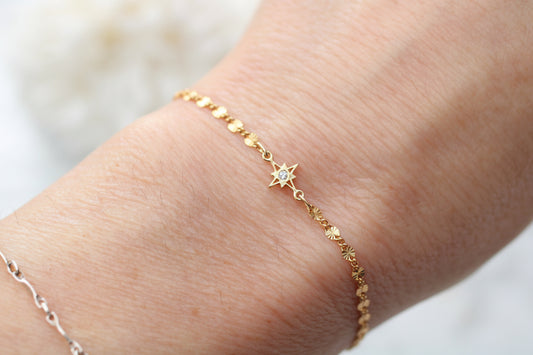 Gold bracelet with star-shaped charm on a wrist against a blurred background