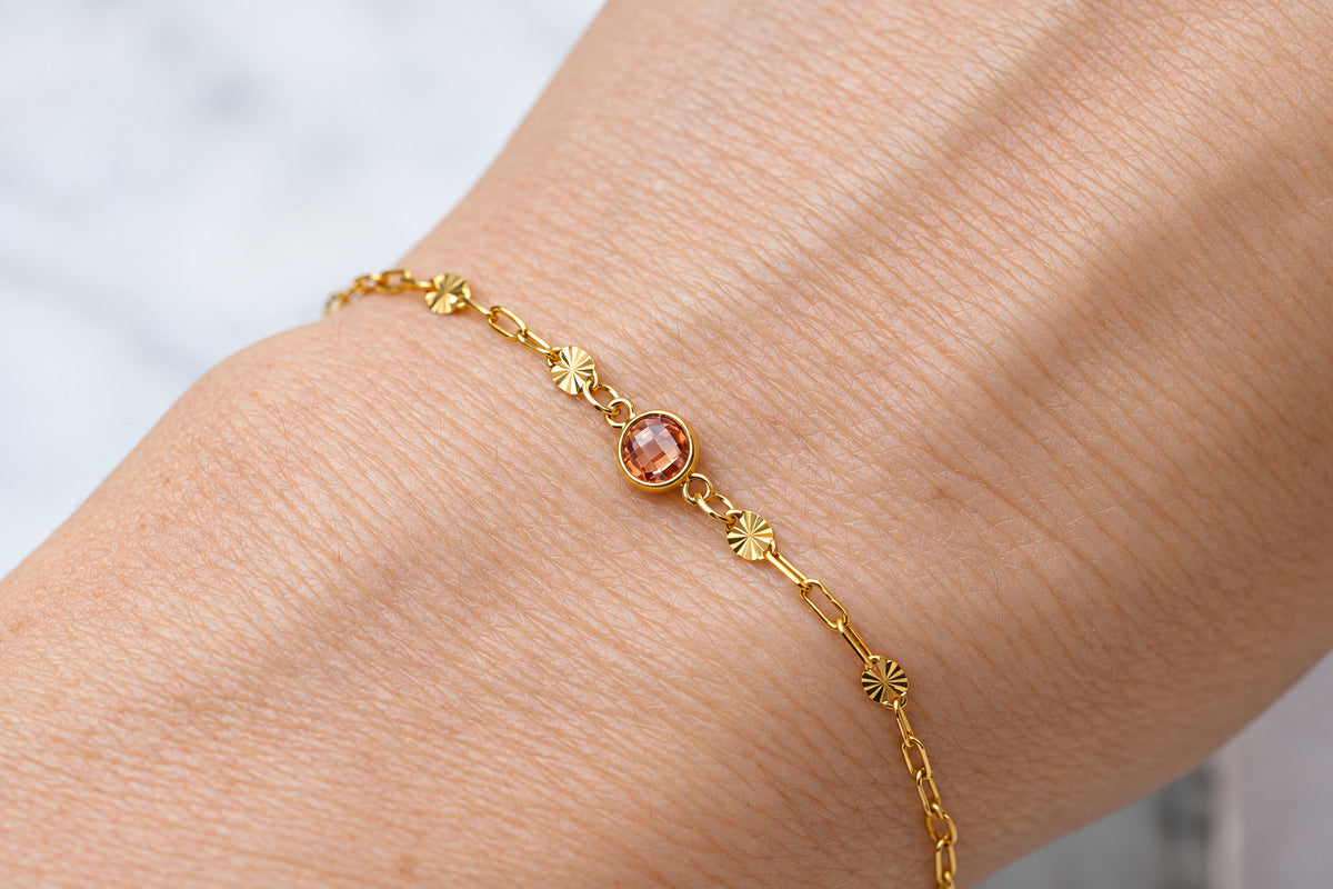 A delicate gold chain bracelet with small starburst charms and a central round amber gemstone, shown worn on a person's wrist.