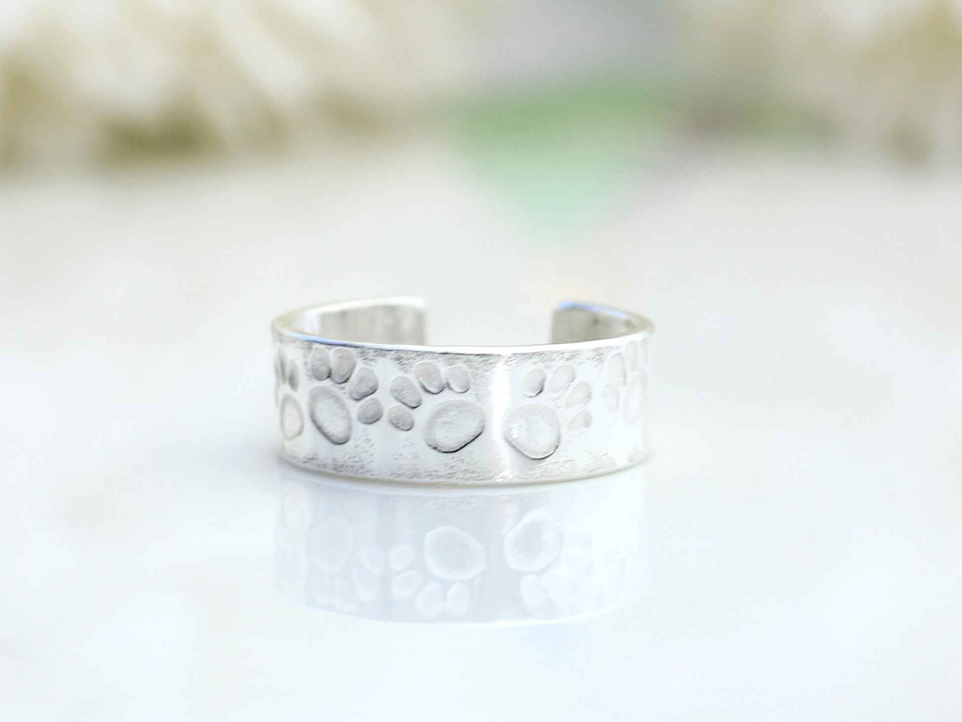A silver ear cuff with a paw print design, displayed on a flat surface.