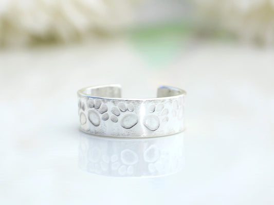 A silver ear cuff with a paw print design, displayed on a flat surface.