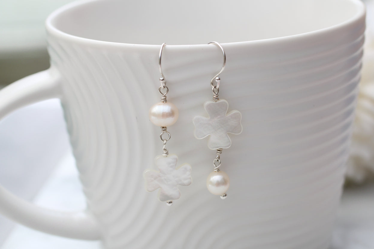 Pearl and flower-shaped earrings on a white cup