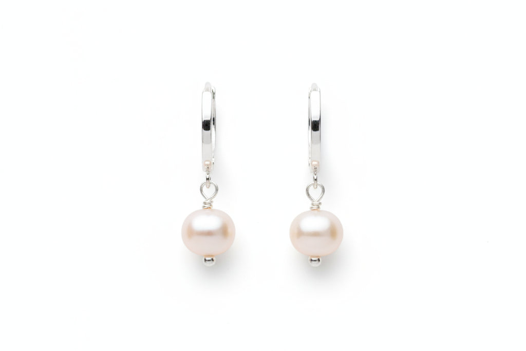 Silver hoop earrings with pearl drops on a marble surface
