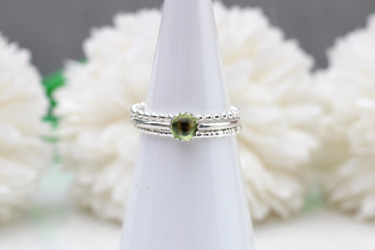 Silver ring with a green gemstone on a white stand against a blurred floral background