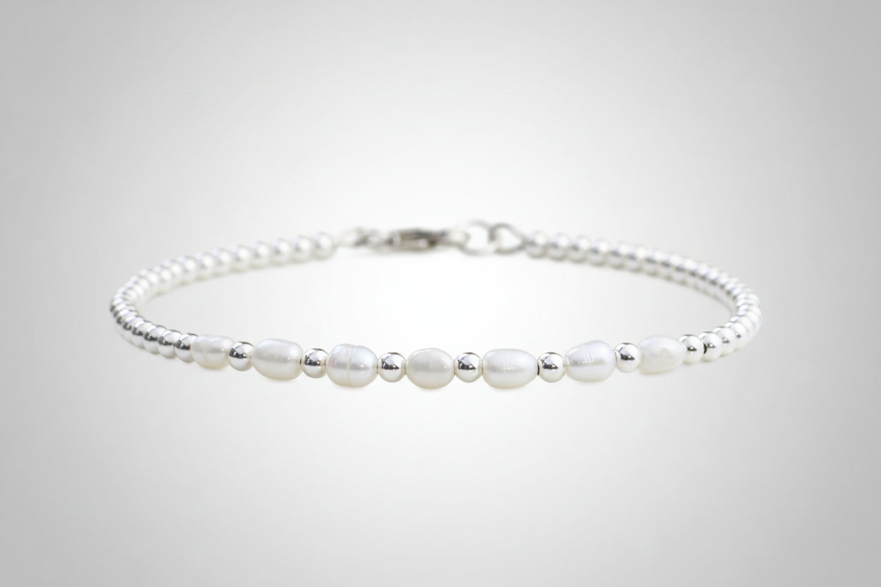 A sterling silver bracelet with freshwater pearl beads, presented against a floral background.