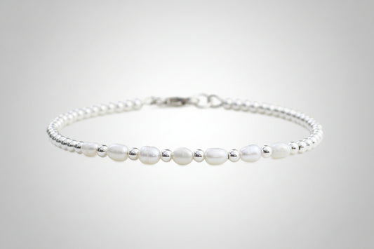 A sterling silver bracelet with freshwater pearl beads, presented against a floral background.