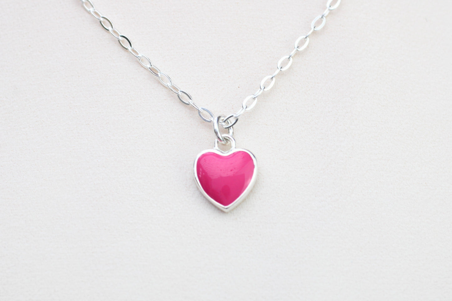 A sterling silver necklace with a pink enamel heart charm.