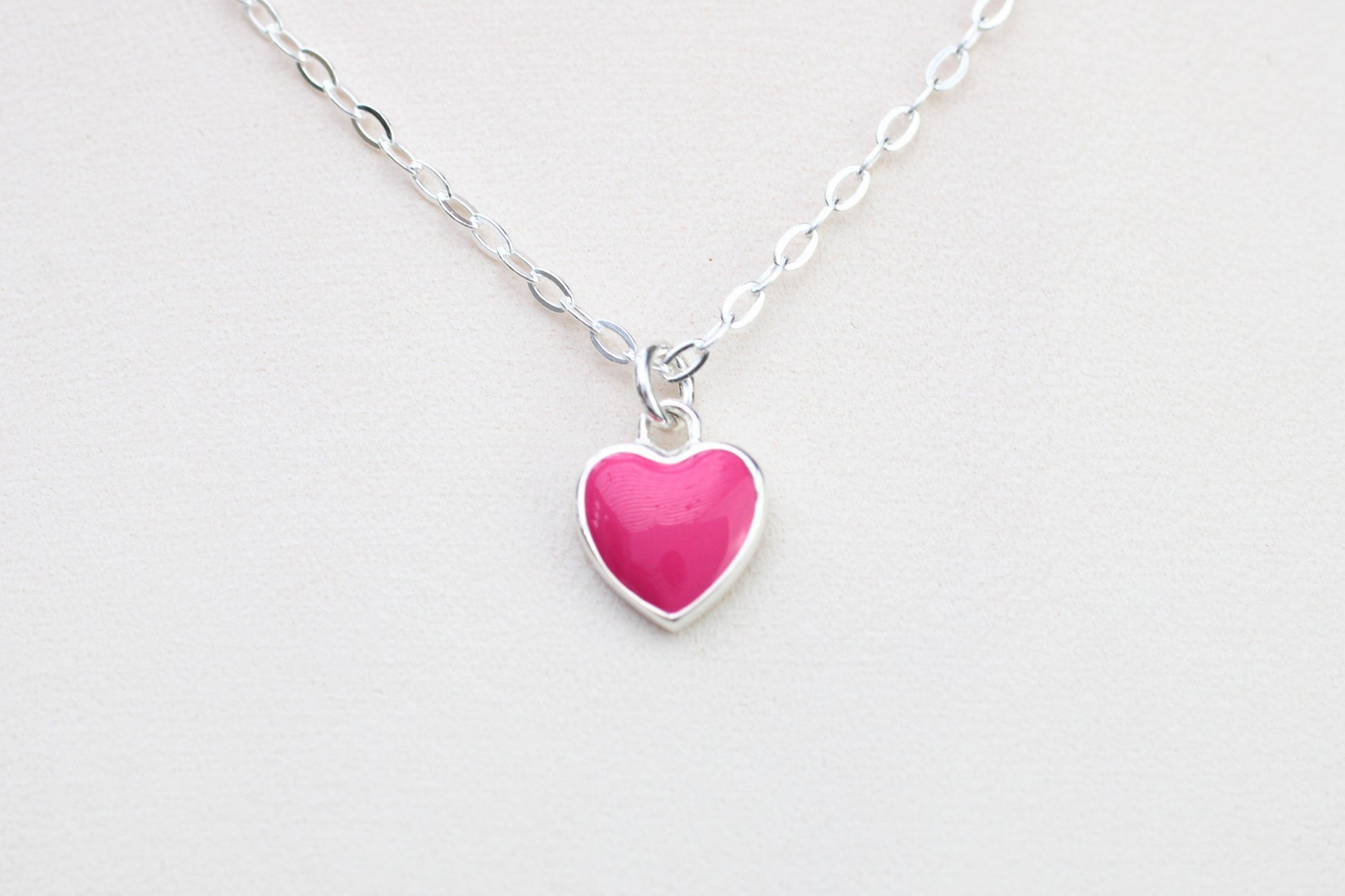 A sterling silver necklace with a pink enamel heart charm.