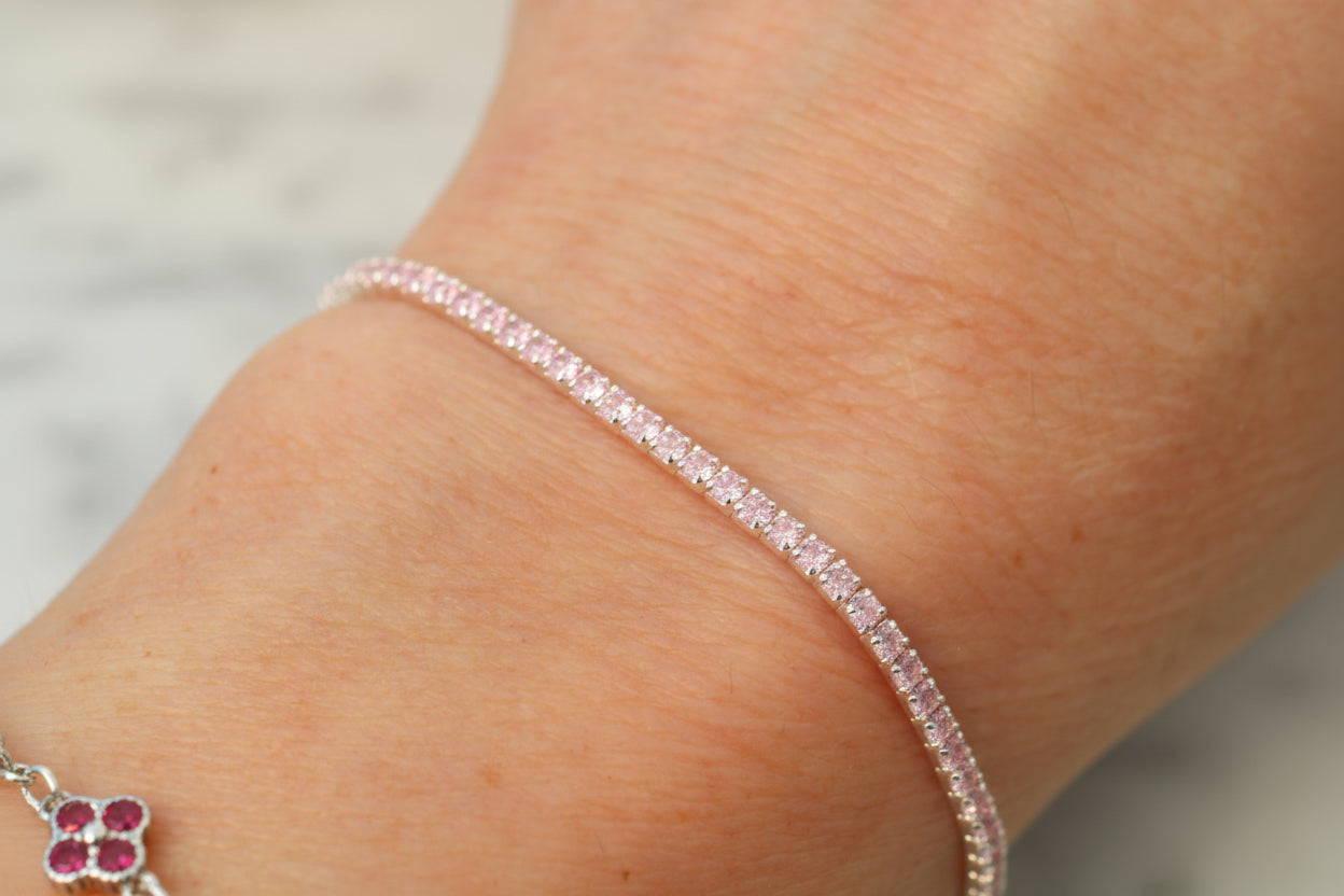 Close-up of a person's wrist wearing a pink tennis bracelet on a neutral background