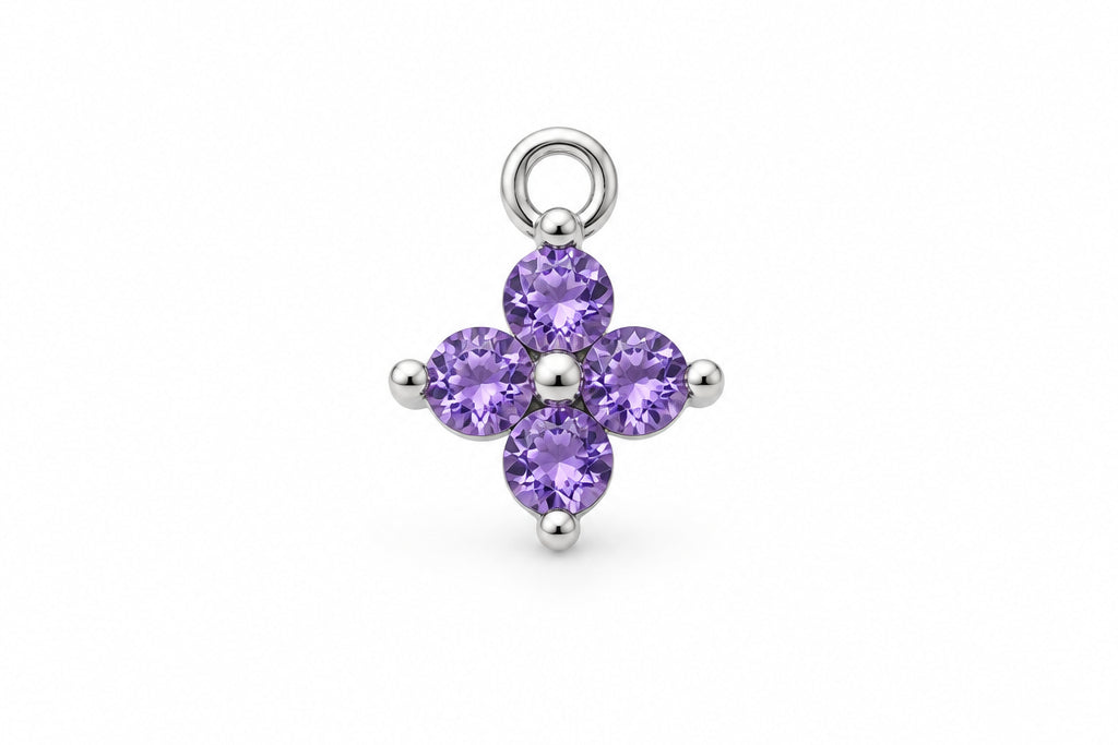 A small silver flower charm with four purple gemstones, displayed on a white marble surface.