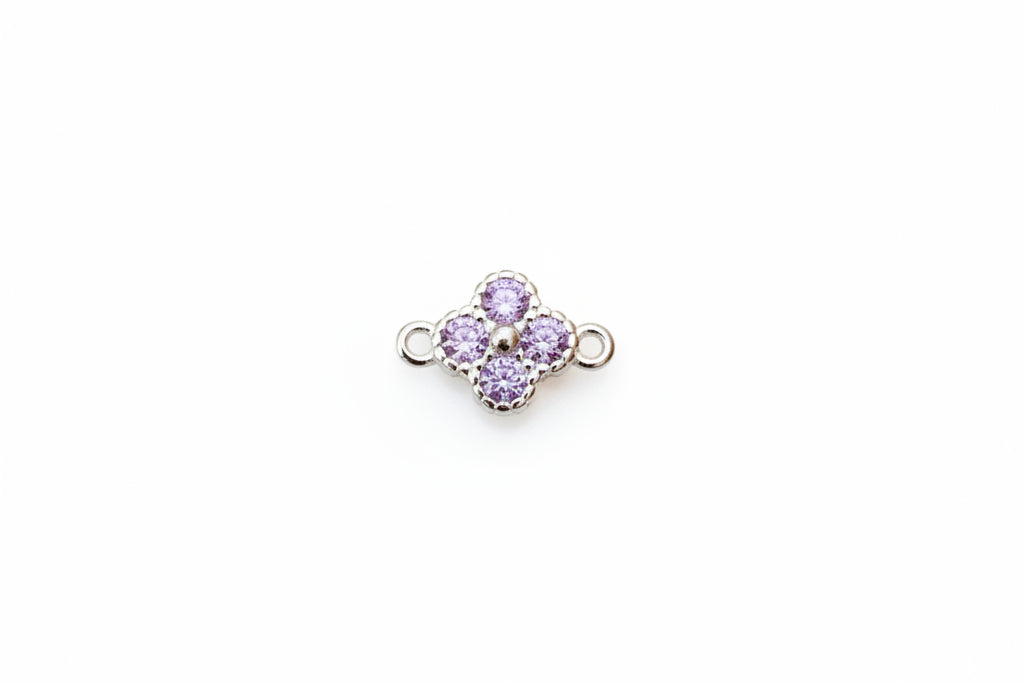 A small silver-tone four-petal flower charm with light purple gemstones, displayed on a white marble surface.