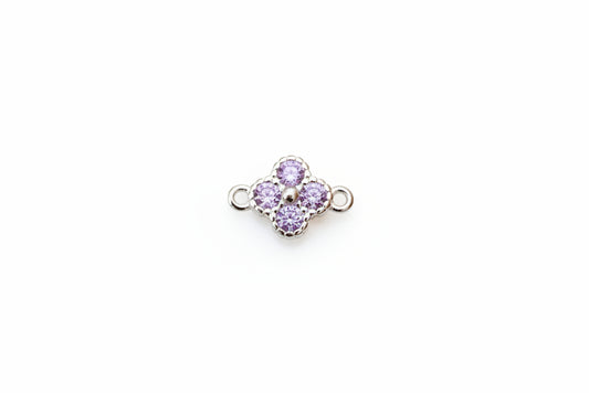 A small silver-tone four-petal flower charm with light purple gemstones, displayed on a white marble surface.