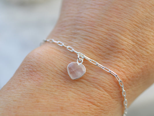 Silver bracelet with a heart-shaped pink stone on a wrist against a blurred background