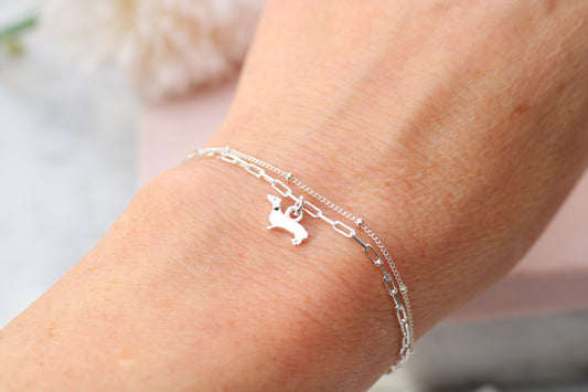 A close-up of a delicate silver chain bracelet with a small rabbit charm, worn on a person's wrist.