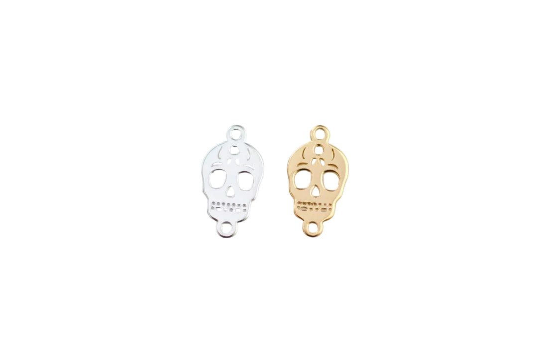 Two skull-shaped pendants, one gold and one silver, on a light gray background.