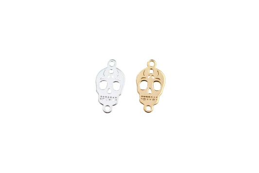 Two skull-shaped pendants, one gold and one silver, on a light gray background.