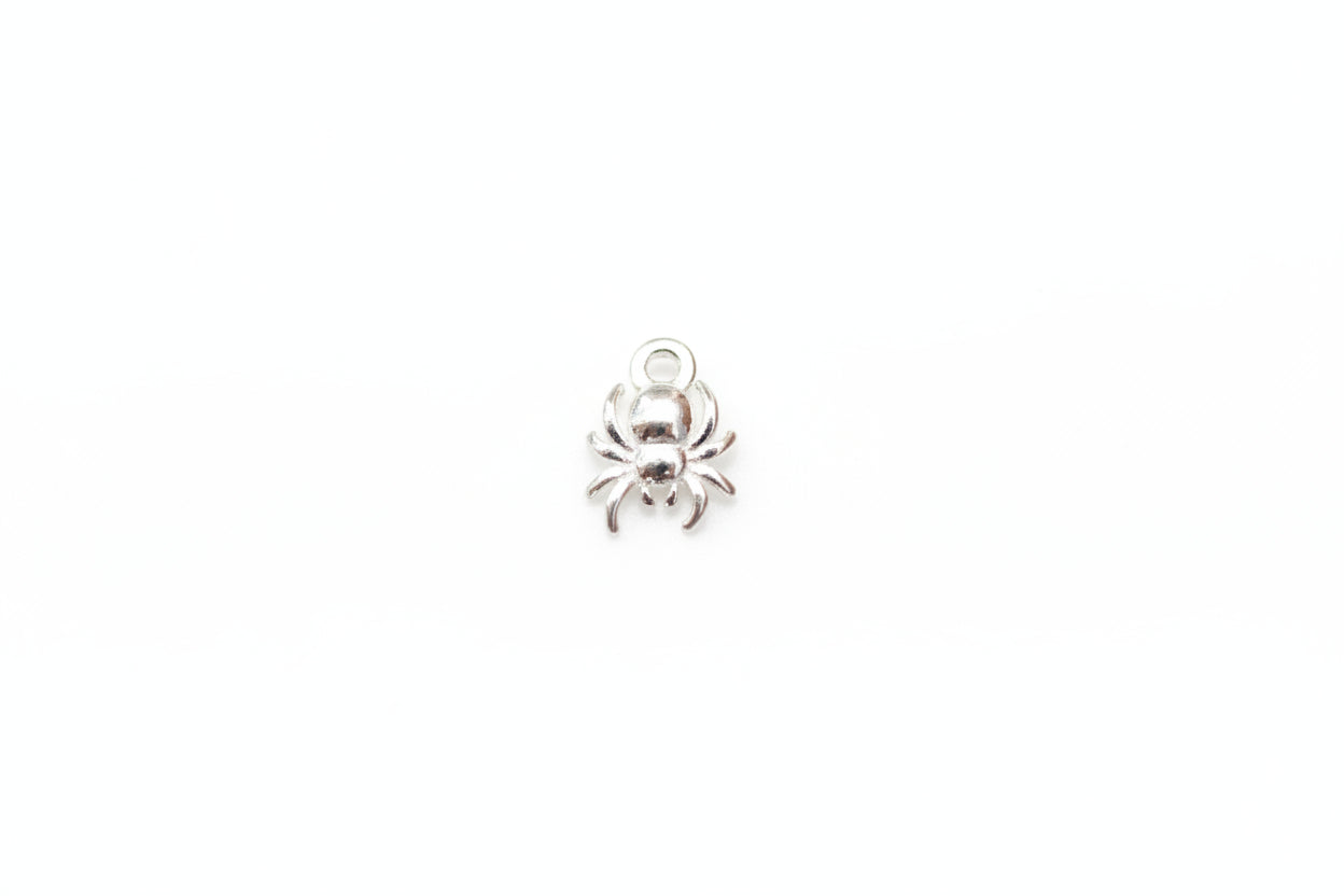 A small silver spider charm with a top loop, resting on a light gray marble surface.