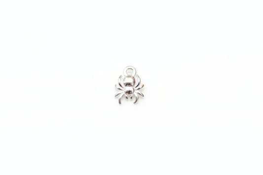 A small silver spider charm with a top loop, resting on a light gray marble surface.