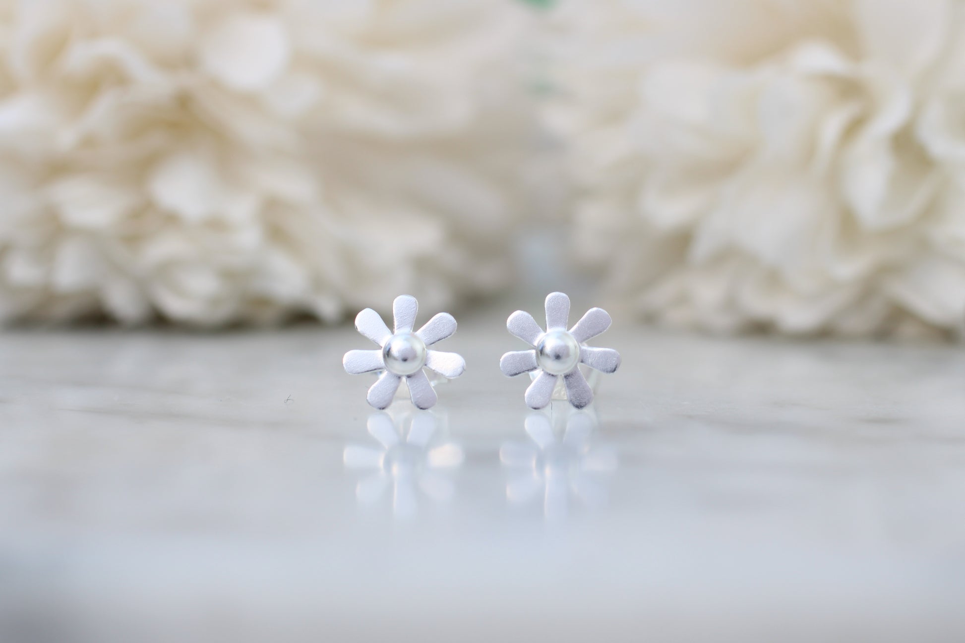 silver flower-shaped earrings on a light background