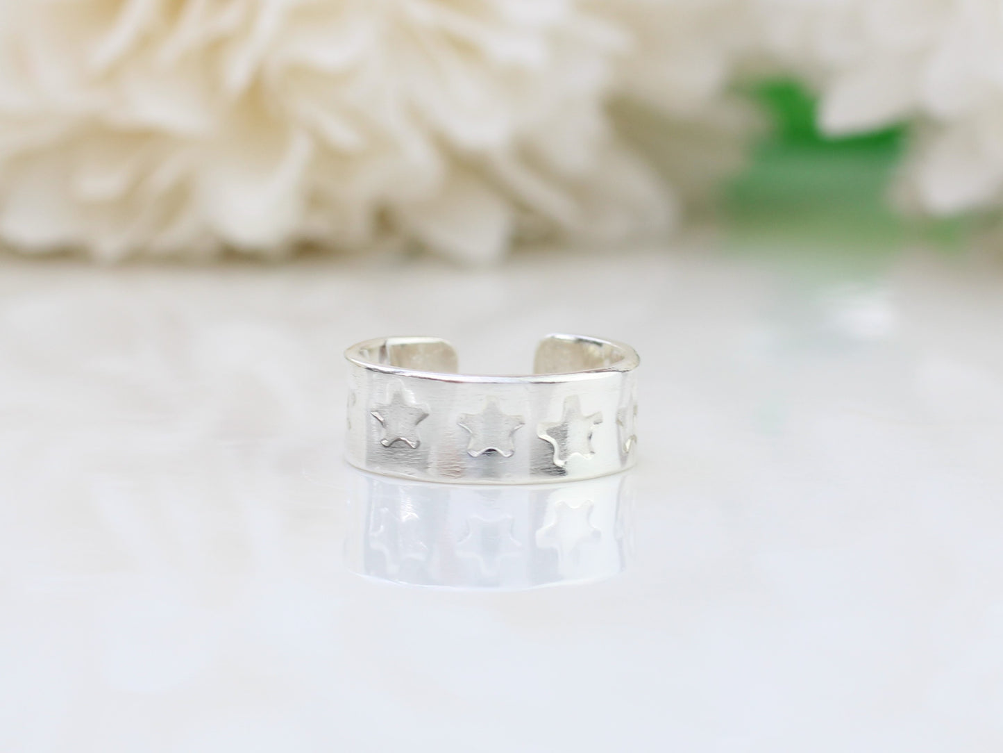 A silver ear cuff with a star pattern, placed on a white surface next to white flowers