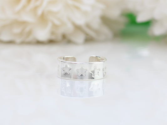 A silver ear cuff with a star pattern, placed on a white surface next to white flowers