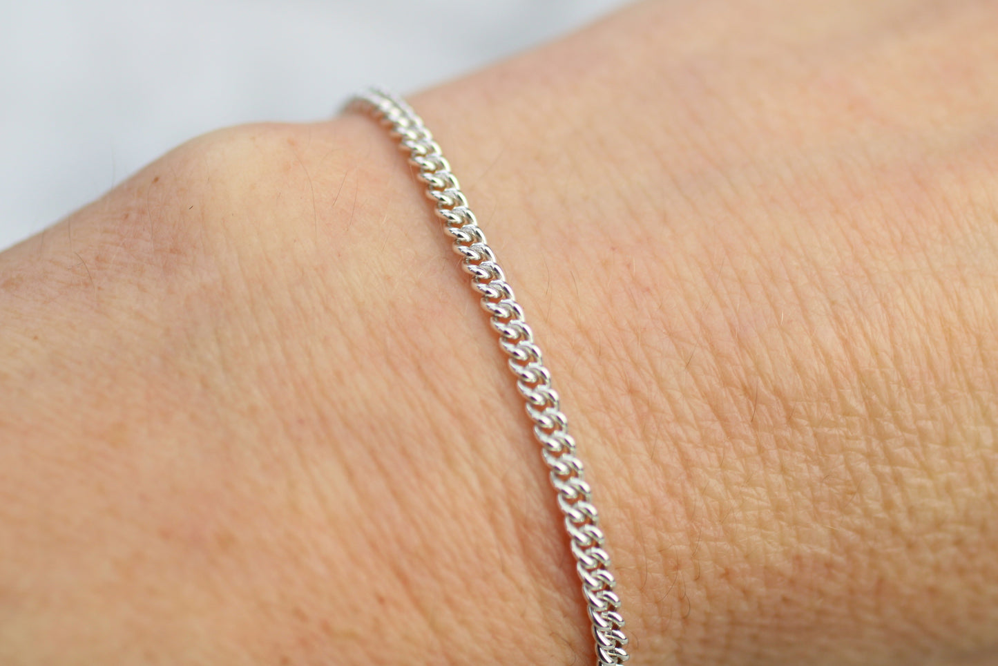 Silver bracelet on a wrist with a plain background