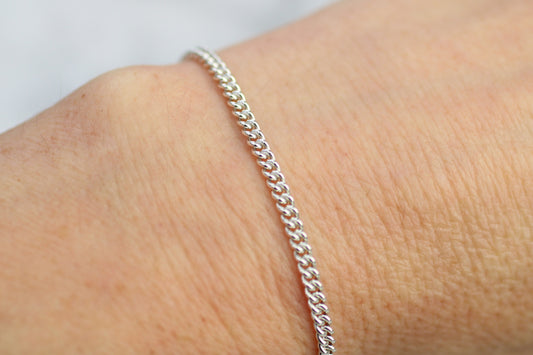 Silver bracelet on a wrist with a plain background