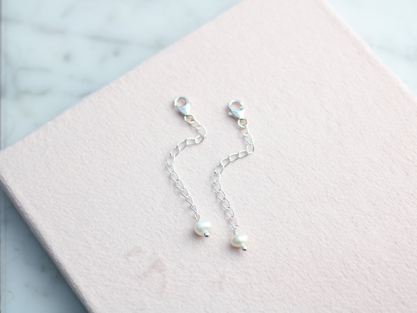Pearl earrings on a pink jewelry box with a light marble background